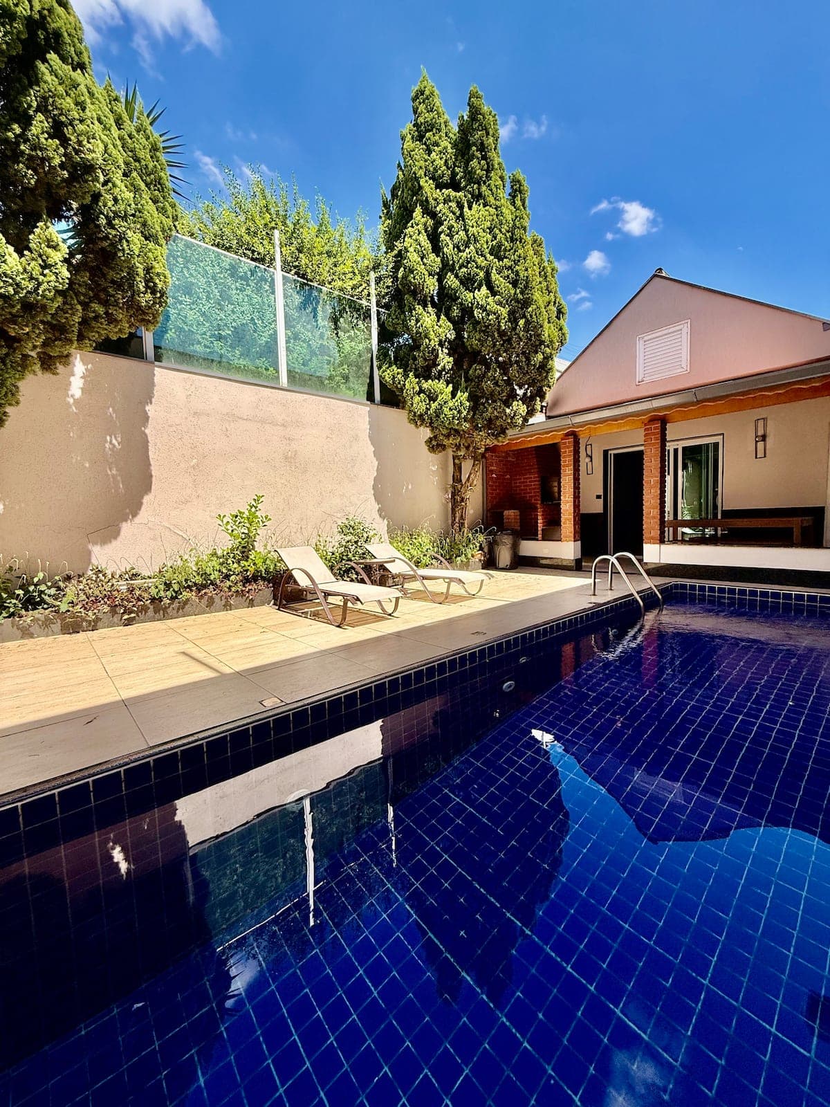 Piscina azul com espreguicadeiras e jardim ao fundo